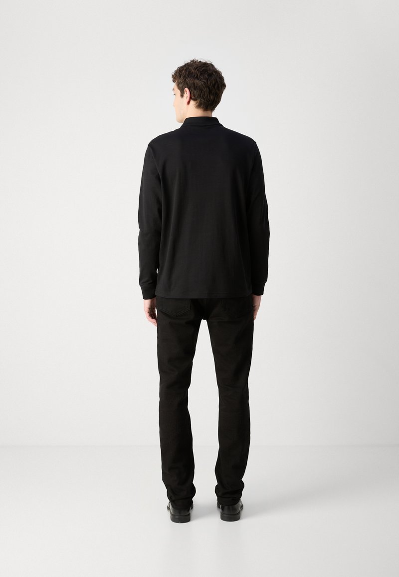 Schwarzes Langarmhemd mit Kragen, kombiniert mit schwarzen Hosen. Schmal geschnittenes Design, glatte Textur, minimalistische Details, von hinten betrachtet.