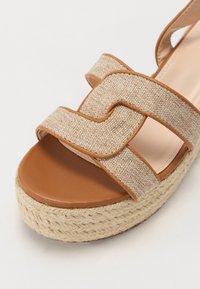 Sandală platformă de culoare bej, cu curele din material texturat, având o talpă din jute împletit și un șezut neted de culoare maro.