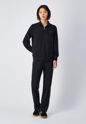 Giacca nera con zip e pantaloni abbinati realizzati in tessuto morbido. La giacca presenta un colletto e un logo. I pantaloni hanno strisce laterali bianche e un fit rilassato.