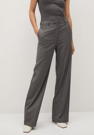 Woman wearing high-waist wide-leg gray trousers and matching sleeveless top, standing with hands in pockets and white square-toe shoes.