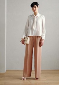Bílá blůza s detaily vázání, v kombinaci s světle růžovými kalhotami s širokými nohavicemi. Hladká tkanina, elegantní design a minimální doplňky.