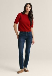 Rød kortærmet sweater, cropped pasform, kombineret med mørkeblå skinny jeans og brune sneakers med hvide snørebånd. Enkel design med tekstureret stof.