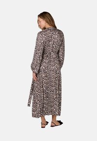 Maxi jurk in een beige en zwarte luipaardprint, met lange mouwen, een strik taille en een vloeiende uitstraling. Gladde textuur met een gelaagde rok.