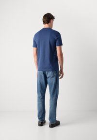 Camiseta de manga corta azul marino con escote redondo, combinada con jeans rectos de color azul claro y zapatos negros, vista desde la espalda.