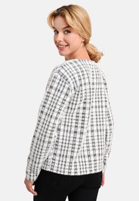 Schwarz-weißer karierter Pullover mit lockerer Passform, runder Ausschnitt und langen Ärmeln. Weicher Stoff und gerippte Bündchen.