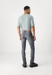Muška svijetloplava majica uparena sa slim-fit sivim trapericama. Traperice imaju vidljivu oznaku i suptilne detalje šivanja, nošene uz tamne tenisice.