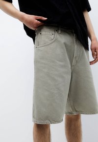 Shorts in denim grigio chiaro con una vestibilità rilassata, tasche frontali e orlo grezzo. Il tessuto ha una finitura opaca e una texture sottile.