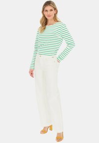 Zielona i biała w paski bluzka z długim rękawem, zestawiona z białymi spodniami o szerokich nogawkach. Zauważalne żółte słupkowe obcasy dopełniają stylizację.