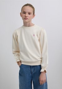 Hanorac crem cu mâneci lungi, guler rotund cu model tip plasă și manșete elastice. Logo mic roz cu craniu pe piept. Croială casual.