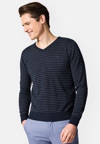 Granatowy sweter z długim rękawem i dekoltem w serek, z jasnoszarymi poziomymi paskami, ściągaczami na mankietach i u dołu oraz małym logo na piersi. Miękka faktura.