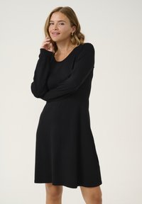 Abito lungo nero a maniche lunghe con scollo a barca e forma svasata a A. Realizzato in tessuto morbido, presenta una semplice cucitura lungo l'orlo e le maniche.