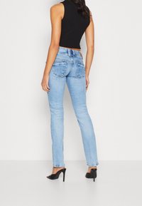 Jeans de color azul claro con una silueta ajustada, ligeramente acampanados en la parte inferior. Con bolsillos traseros con costuras curvas y una cintura de altura media.