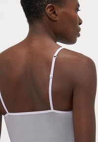 Camisola lilla con spalline sottili regolabili, che presenta una trama liscia e trasparente. Il design aderente mette in risalto la schiena e l'area delle spalle.