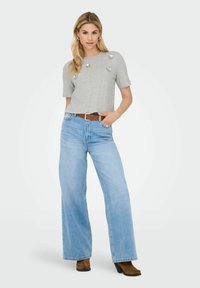 Maglietta grigia a maniche corte con pietre decorative, abbinata a jeans a gamba larga di un blu chiaro e una cintura marrone, con una vestibilità casual.