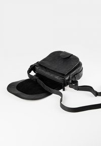 Musta nahkainen olkalaukku sileällä pinnalla, pyöristetty pää, vetoketjukiinnitys ja säädettävä hihna. Vuorattu sisus pehmeällä tekstuurilla.