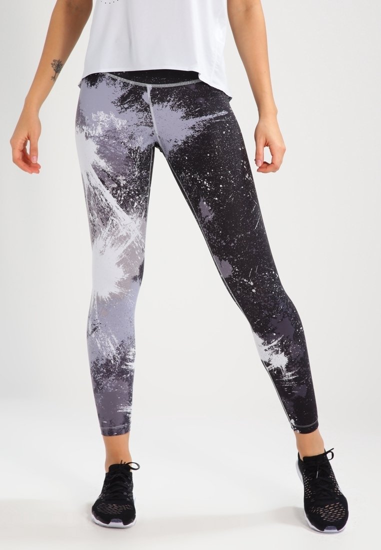 Leggings de fitness avec un design éclaboussé noir et gris, dotés d'une taille haute et d'un tissu extensible pour plus de confort. Des chaussures de sport noires sont portées.