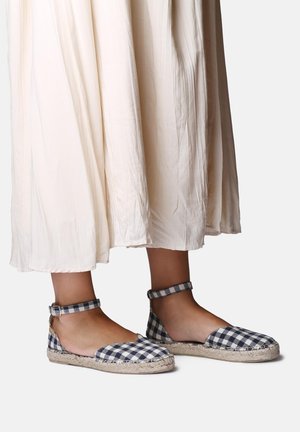 Stopy w czarno-białych espadrylach z kostką na pasku, zestawione z lekką, kremową plisowaną spódnicą.