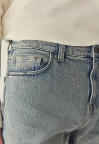 Lichtblauwe spijkerbroek met een licht versleten look, uitgerust met een ontwerp van vijf zakken en een taille op middelhoogte, gecombineerd met een beige trui.