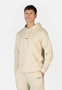 Beige hættebluse lavet af blødt stof, med en forlommelomme og snore. Brandnavnet "BALR." er broderet på brystet.