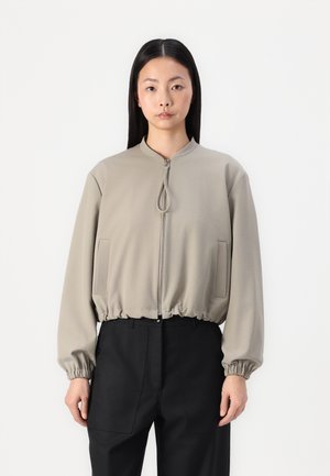 Giacca bomber zip con un leggero beige, con orlo e polsini elasticizzati, dotata di due tasche laterali e colletto rialzato. Tessuto dalla superficie morbida.