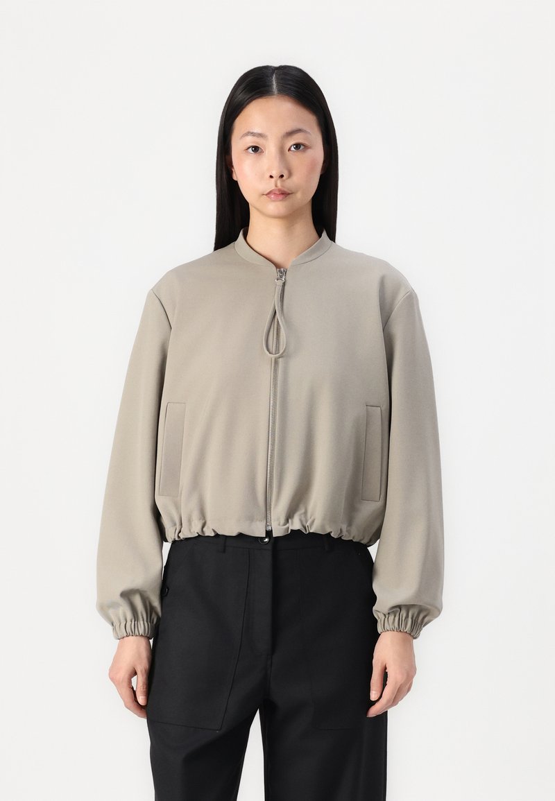 Giacca bomber zip con un leggero beige, con orlo e polsini elasticizzati, dotata di due tasche laterali e colletto rialzato. Tessuto dalla superficie morbida.