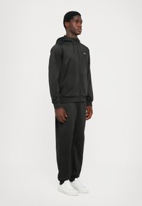 Svart idrottshoodie, har en framficka, justerbar huva och ribbade ärmslut. Matcher med svarta byxor och vita sneakers.