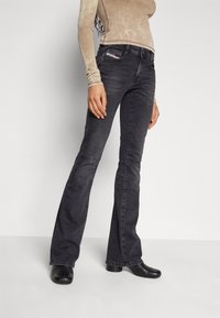 Czarne dżinsy w fasonie dzwonów, z kieszeniami z przodu i subtelnymi detalami przeszycia. Połączone z jasną bluzką z długim rękawem.