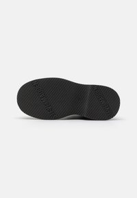Suela de zapato de goma negra con estriado horizontal y nombre de la marca en relieve. Presenta una forma redondeada y un perfil plano para mayor estabilidad.