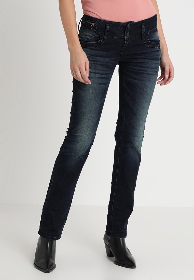 Mörkblå denimjeans med smal passform, subtila blekningar, fem fickor och metallknappsstängning. Parar med svarta högklackade stövlar.