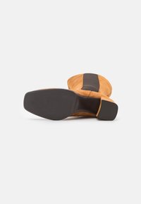 Wildleder-Stiefelette in Tan mit einem schwarzen strukturierten Panel. Flache Gummisohle und runde Spitze. Innen leicht gepolstert für zusätzlichen Komfort.