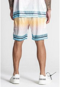 Lettere shorts med en gradientfarve fra hvid til orange, prydet med en blå mønstret kant ved kanten. Båret med hvide sneakers.