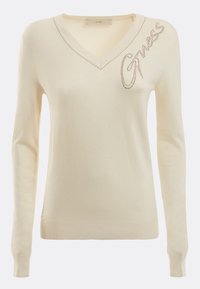 Pull crème avec col en V, manches longues, poignets côtelés et un logo décoratif "Guess" orné de strass. Texture en maille douce.