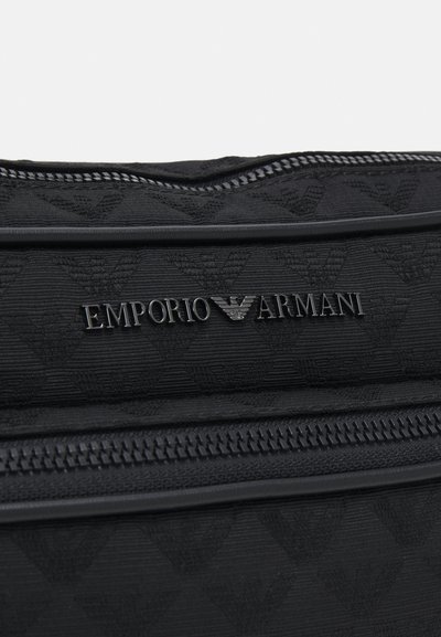 Melnas auduma soma ar teksturētu rakstu, iegravētu zīmolu "EMPORIO ARMANI" un gludu rāvējslēdzēja akcentu pa malu.