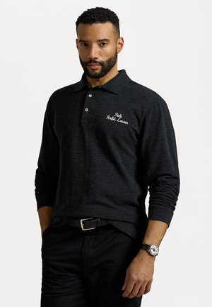 Dunkelgraues Langarm-Polohemd mit einem Knopfleiste mit drei Knöpfen und gesticktem Logo auf der linken Seite. Kombiniert mit schwarzen Hosen und einer Uhr.
