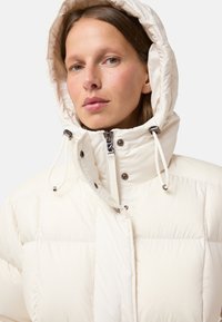 Puff jacket in off-white, featuring a hood, zip closure, and metallic accents. The fabric is smooth with a quilted pattern for insulation.