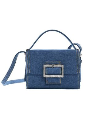 Bolso de mezclilla azul con asa superior, correa de hombro desmontable y gran hebilla rectangular de pedrería en la solapa frontal.