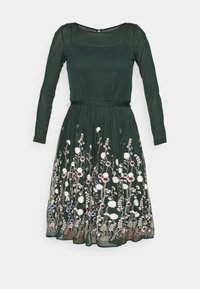 Grünes Kleid mit langen durchsichtigen Ärmeln, quadratischem Ausschnitt, einer enganliegenden Oberseite und einem schwingenden Rock. Mit floralen Stickereien in Weiß, Lila und Pink.