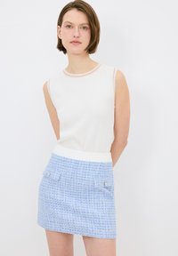 Valkoinen hihaton paita, jossa on vaaleanpunaiset reunat, yhdistettynä vaaleansiniseen kuvioituun mini-hameseen, joka sisältää kaksi etutaskua ja hopeisia nappikoristeita.