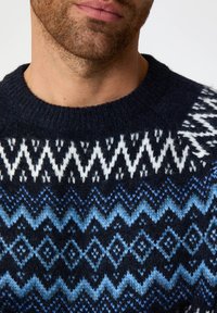 Dunkelblauer Pullover mit strukturiertem Strickmuster. Mit Zickzack- und Diamantmotiven in Blau- und Weißtönen. Klassischer Rundhalsausschnitt.