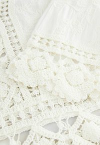 White crochet fabric featuring intricate floral patterns and lace edges, with a soft texture and detailed stitching.