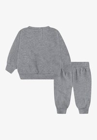 Conjunto de sudadera y pantalones de chándal gris, con tela suave, puños acanalados y ajuste relajado. La parte superior tiene un cierre en la parte posterior y un diseño minimalista.
