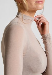Lichtbeige langemouwtop met een hoge hals, gemaakt van doorschijnende, rekbare stof. Heeft aangesloten mouwen en een gladde textuur.