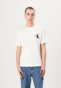 White cotton t-shirt featuring a black "cK" logo on the left chest. Classic crew neck design, short sleeves, and relaxed fit.