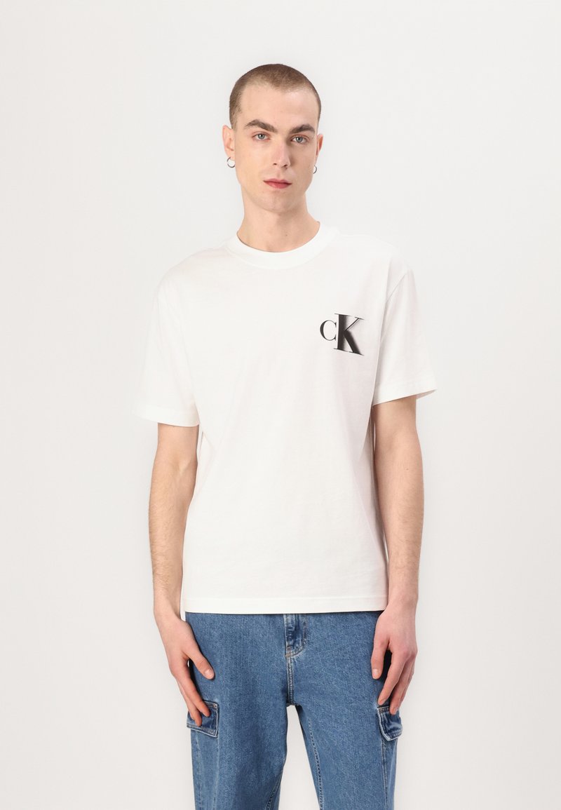 White cotton t-shirt featuring a black "cK" logo on the left chest. Classic crew neck design, short sleeves, and relaxed fit.