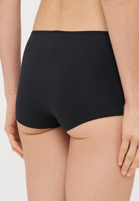 Černé bavlněné hipster šortky s hladkou texturou, s jednoduchým designem a bez viditelných vzorů nebo kovových prvků, z pohledu zezadu.