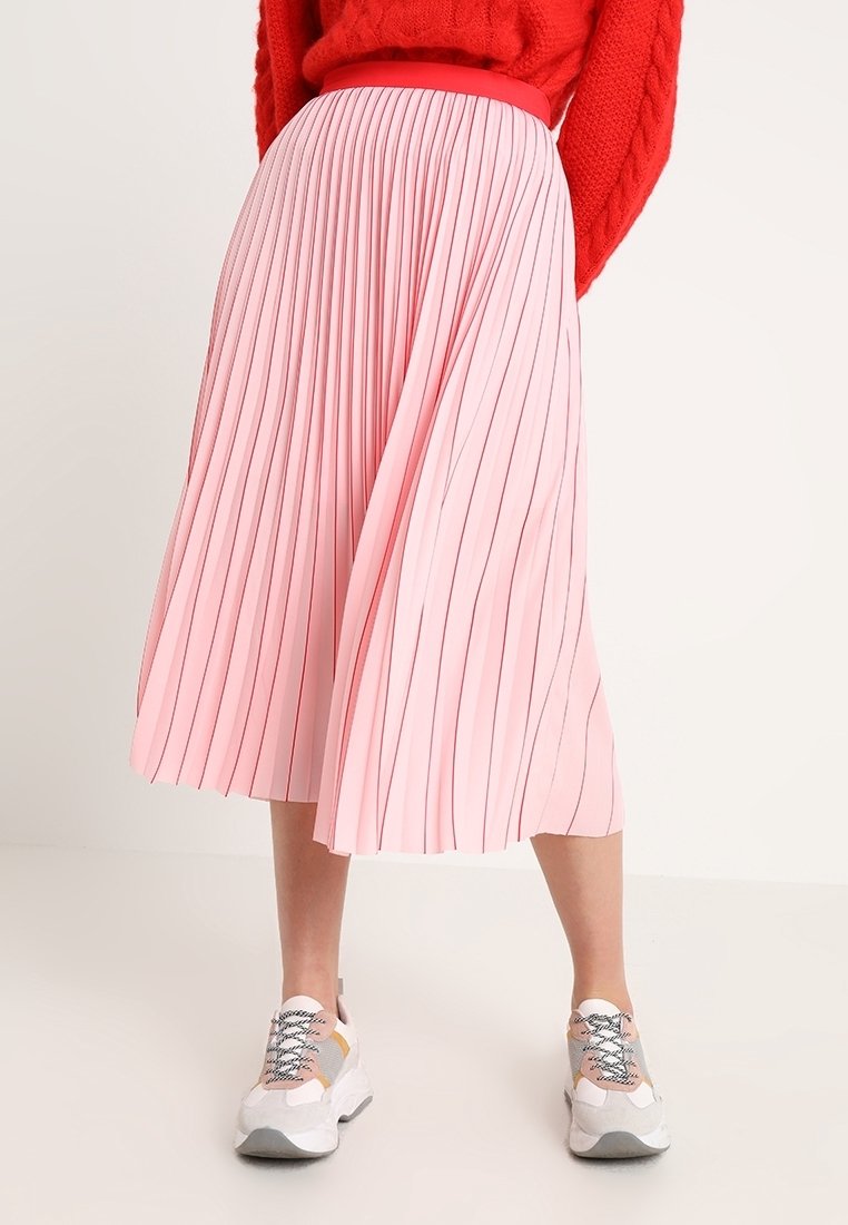 Jupe midi plissée en rose pâle avec des rayures verticales, dotée d'une taille ajustée. Associée à des baskets chunky de couleurs claires.