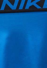 Μαύρη ζώνη μέσης Nike με μπλε κείμενο πάνω από έντονο μπλε ύφασμα, πιθανώς μέρος αθλητικής ένδυσης.