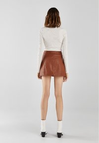 Hnědá kožená mini sukně s rozšířeným střihem a hladkou texturou, v kombinaci s přiléhavým bílým žebrovaným topem s dlouhým rukávem a bílými botami na podpatku.