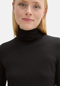 Schwarzes Rollkragenoberteil aus einem dehnbaren, glatten Stoff, mit einem figurbetonten Design und hohem Kragen, geeignet für das Tragen in Schichten oder als eigenständiges Kleidungsstück.