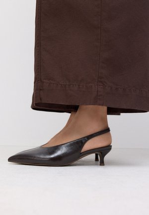 Fekete bőr slingback alacsony kecsketalpú cipő, barna, széles szárú, rövidített nadrággal, egyszínű háttér előtt.